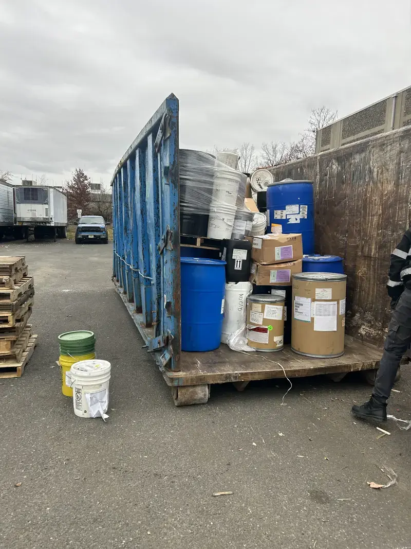 Industrial Waste & Drum Disposal | Safe, Compliant Hauling for Businesses & Contractors Blue dumpster and pallet stacked with industrial barrels and containers for safe hazardous waste disposal